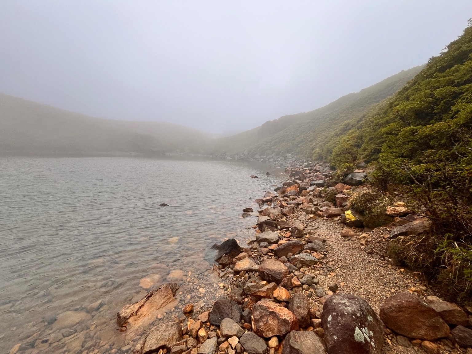 ガスに包まれたくじゅう連山の池と岩の多い岸辺